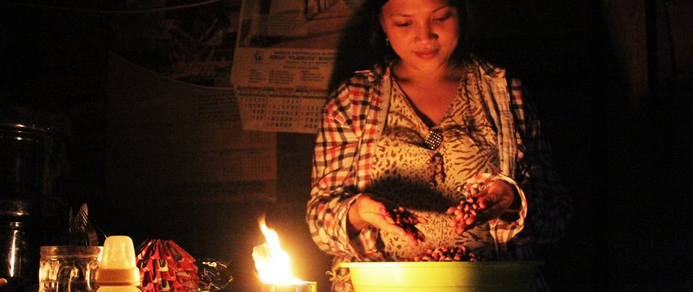 Sandy, a beneficiary of her local Compassion project in Indonesia, sorts beans in her kitchen by hand-made candle light. The hand-made candle was made from an empty metal food can during a workshop at the project.