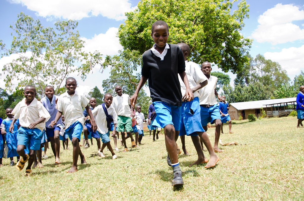 Juliius Otieno Oyalo runs with his friends happily outside in the green grass