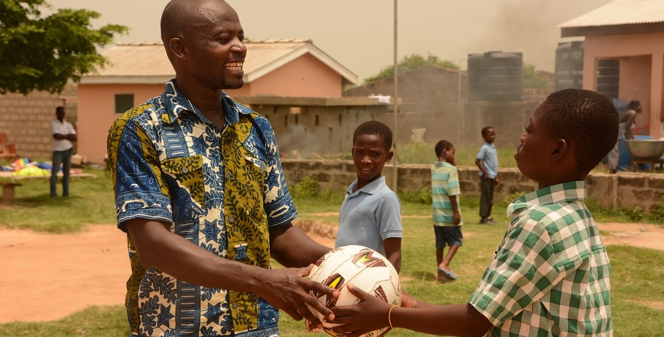 Compassion project worker Henry hands ball to a child